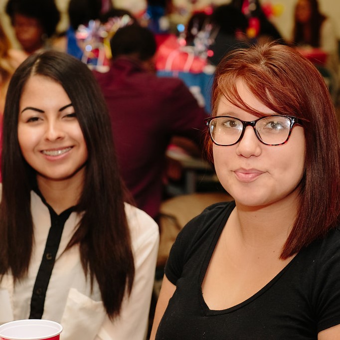 Two young ladies sitting at a table smiling and posing at a party