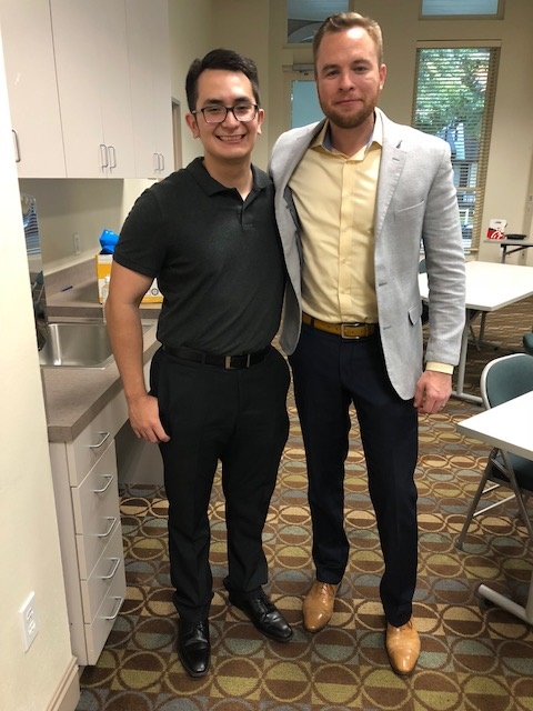 Two sharply dressed men smiling and posing in lunch room