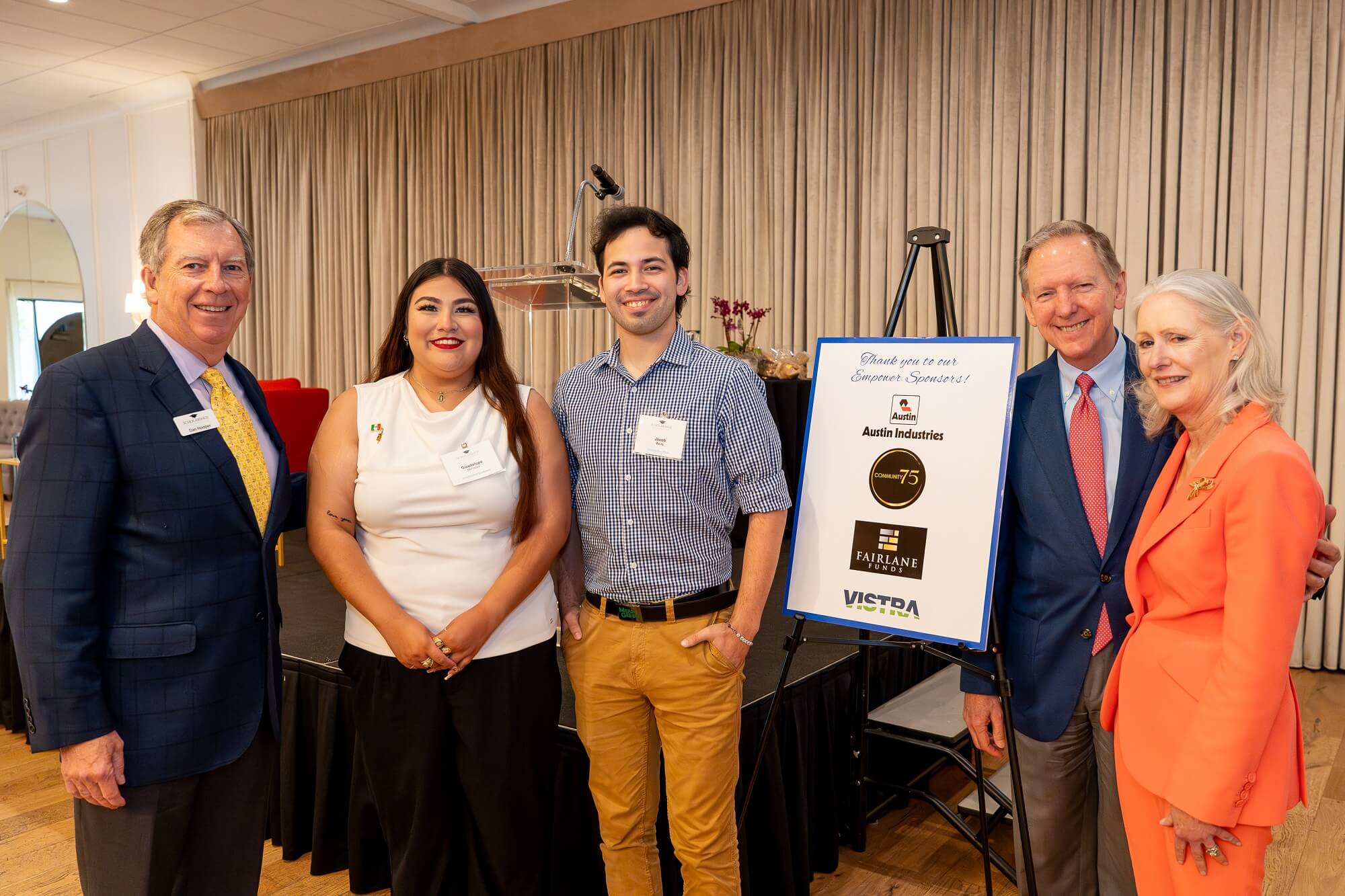 Nicely dressed women and men smiling and posing inside banquet ballroom